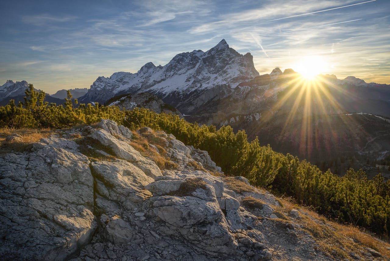 Stunning sunrise casting rays over the Italian Alps in Alleghe, Veneto, with lush greenery and rocky terrain.